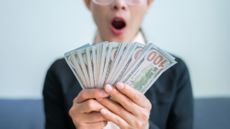Woman excitedly holding a stack of one hundred dollar bills in her hands