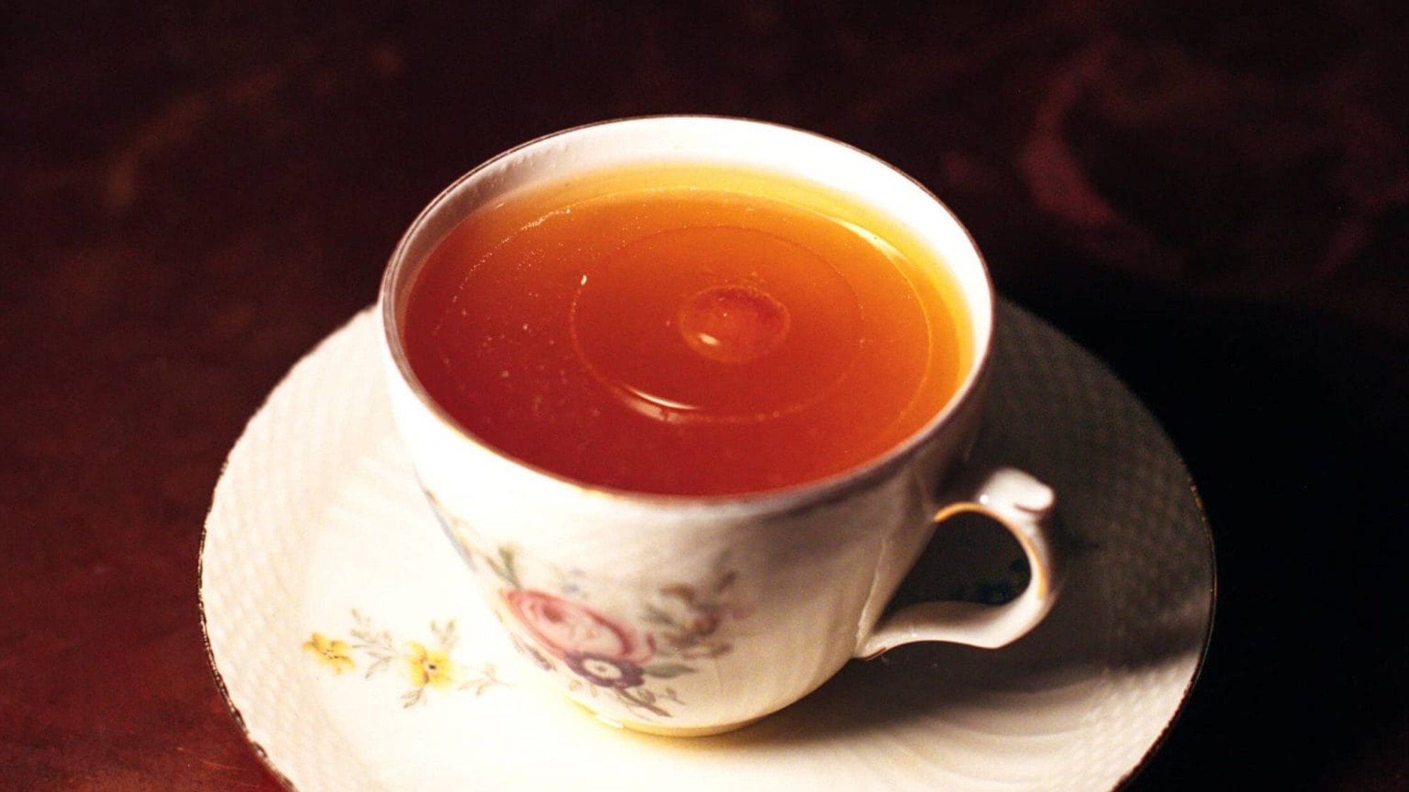 3/4 shot of a fine china mug, filled with a light brown liquid. the mug sits on a complementary frilly edged white saucer