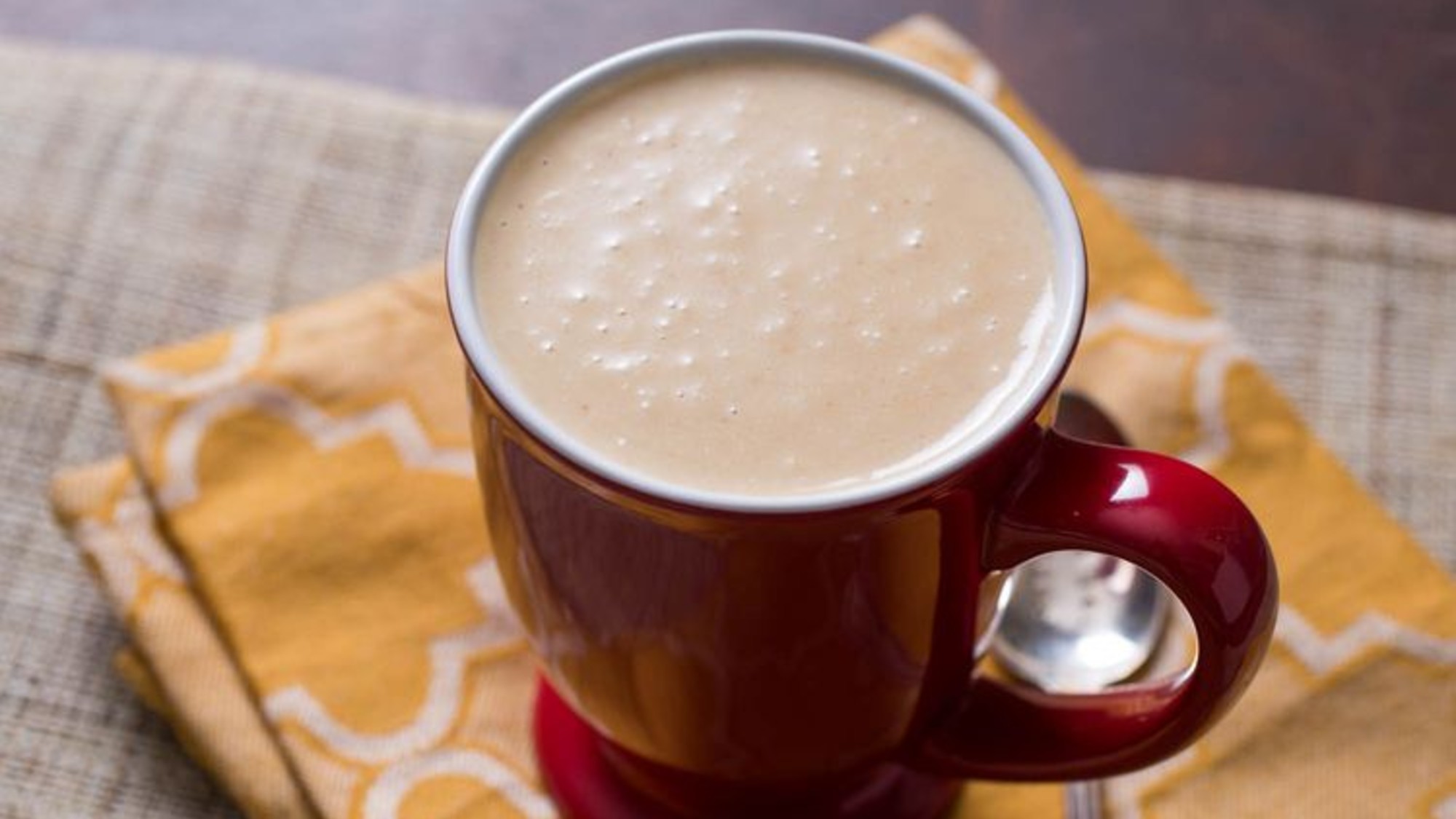overhead shot of a creamy brown liquid in a red mug. the mud sits on a yellow napkin