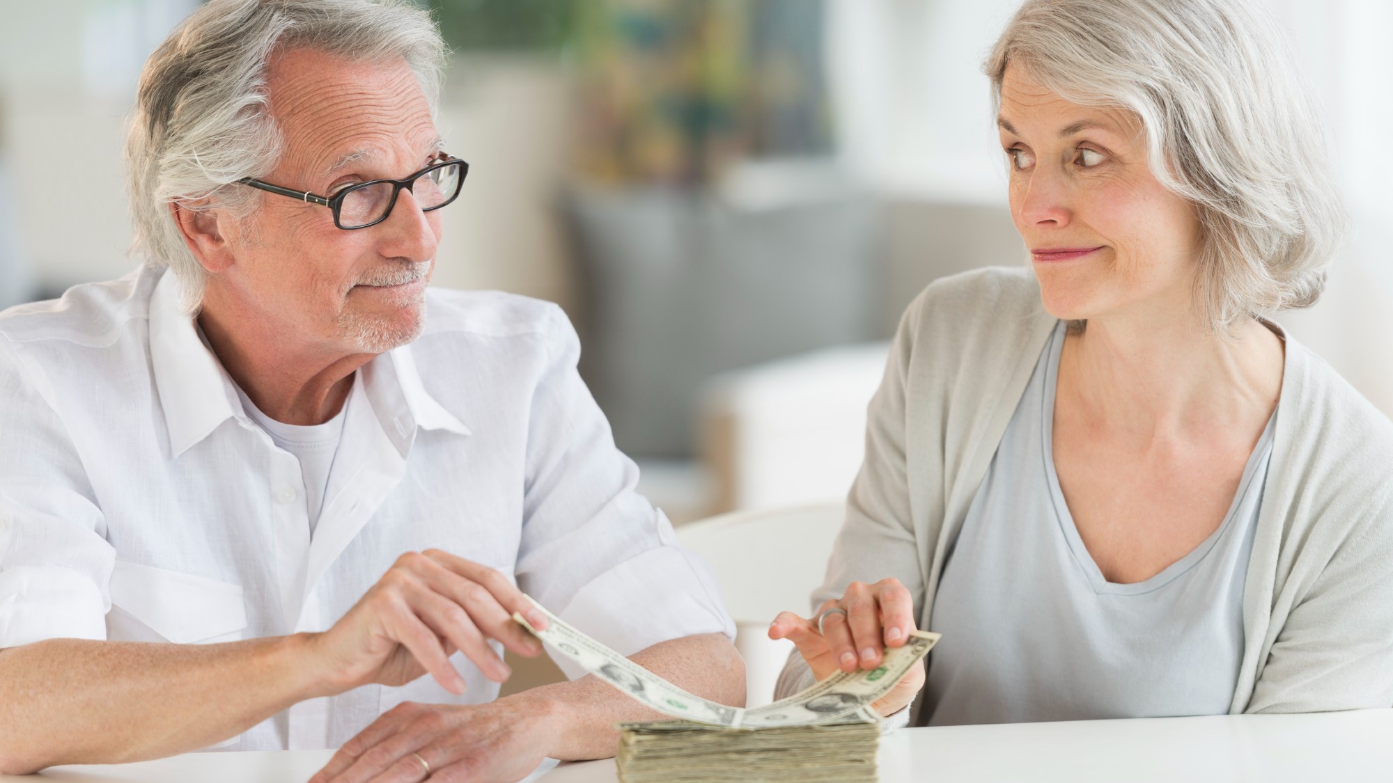 Senior couple looking at each other while pulling dollar bills from a stack of money 