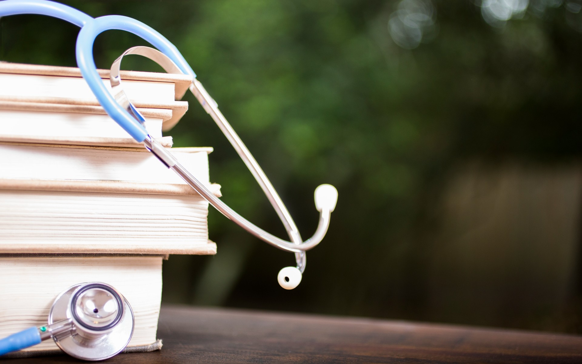 Close-up view of a blue and silver doctor's stethoscope on top of a stack of medical textbooks