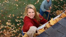 A woman standing on a ladder and cleaning leaves out of her home's gutter