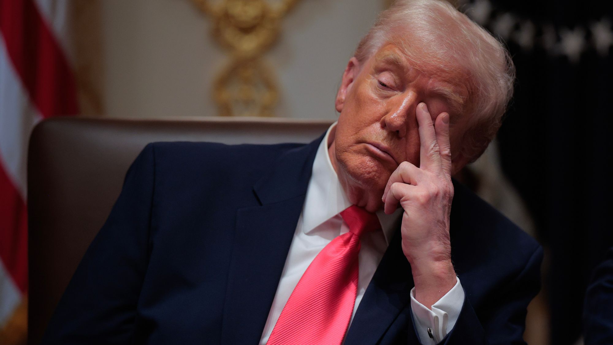 Trump resting against arm of chair he is seated in, with two fingers covering one eye