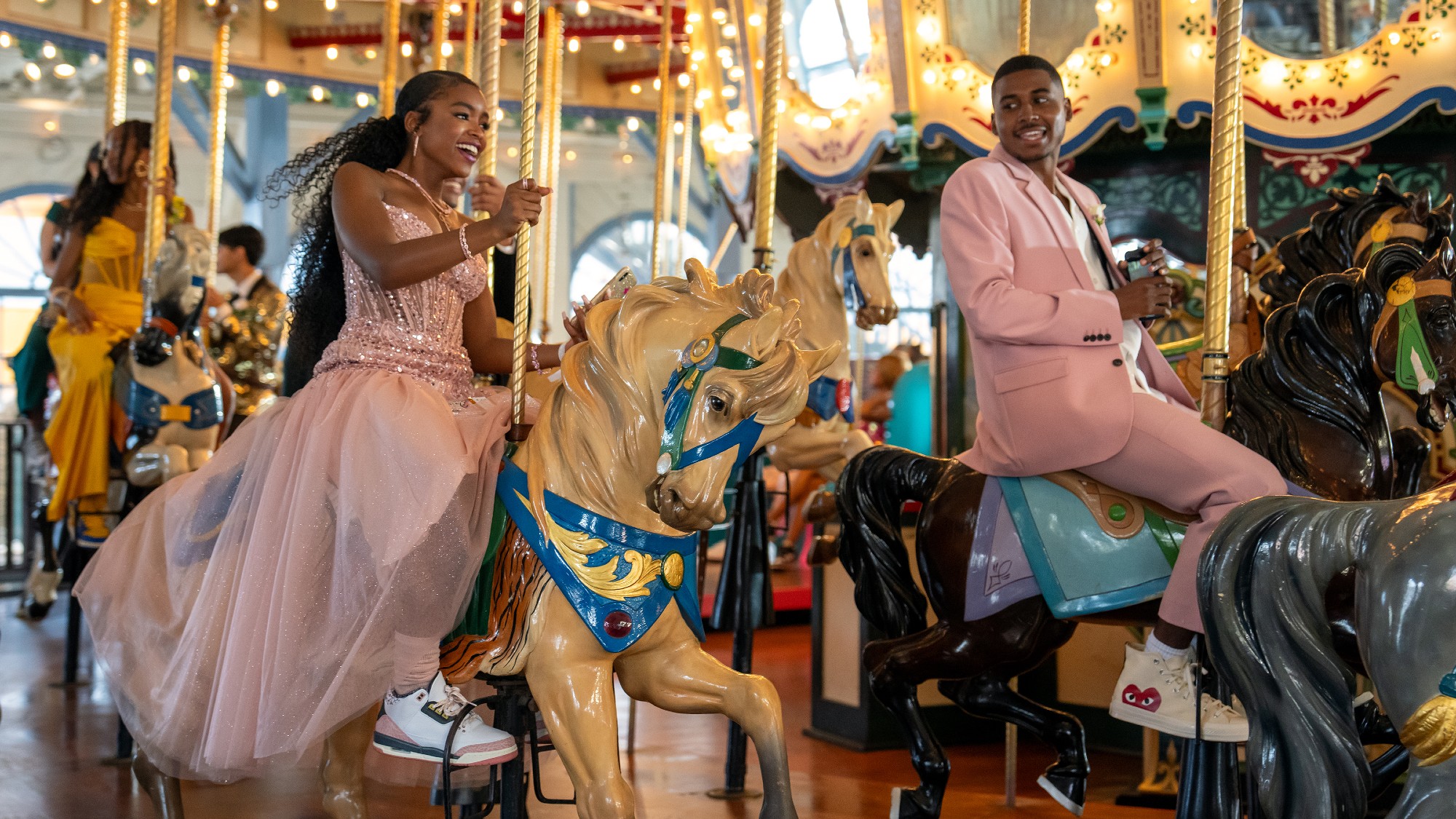 two two lead characters from the show Forever are dressed up in pink outfits. they are riding horses on a carousel ride